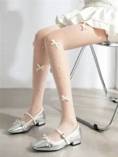 Person wearing white tights with bows and pearls, silver mary jane shoes, and a white dress