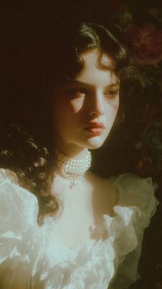 Woman with long dark hair and a pearl choker in a white dress