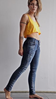 Woman in a yellow crop top and embroidered skinny jeans standing barefoot indoors