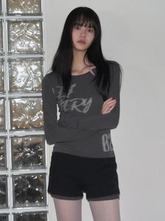 Woman with long black hair and bangs wearing a long sleeve shirt and shorts indoors