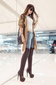 Woman in a trench coat, jeans, and thigh-high boots indoors