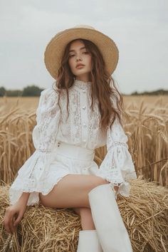 Woman in a white lace outfit and straw hat sitting in a wheat field