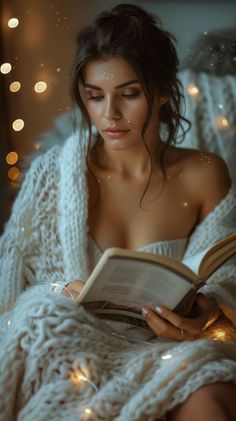 Woman wrapped in a chunky knit blanket reading a book with fairy lights