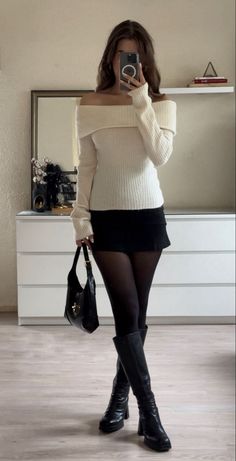 Woman in an off-shoulder top, black mini skirt, and long boots taking a mirror selfie