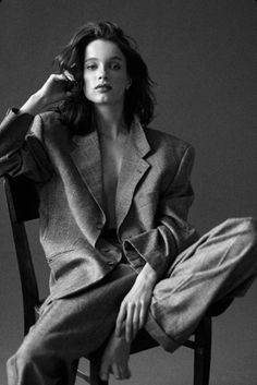 Woman in an oversized suit jacket and pants, sitting barefoot in a studio