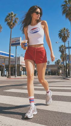 Woman in red shorts and a crop top walking across a street on a sunny day