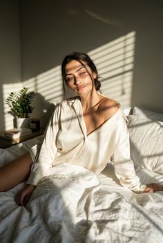 Woman in a white shirt sitting on a bed with natural light and shadows