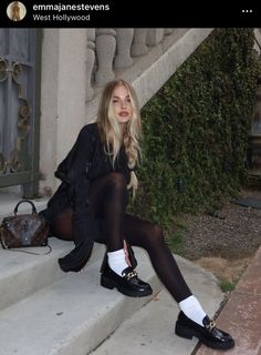 Woman with blonde hair sitting on outdoor steps in a black dress and tights