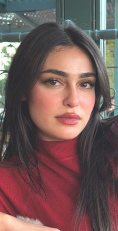 Woman with long dark hair wearing a red turtleneck, looking directly at the camera
