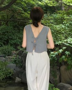 Woman with a ponytail wearing a sleeveless top with an open back and white pants outdoors