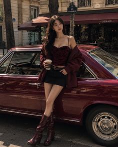 Woman in a mini skirt and crop top leaning against a red car on a street