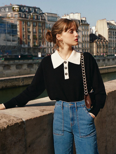 Woman in a black sweater and blue jeans standing outdoors in a city