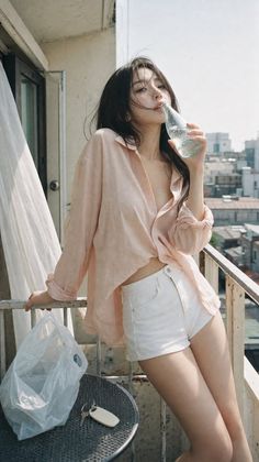Woman in a pink shirt and white shorts drinking from a bottle on a balcony