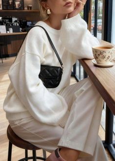 Person in a white sweater and quilted bag sitting at a coffee shop