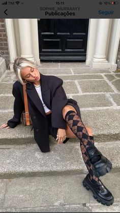 Woman with blonde hair in a black blazer and argyle socks sitting on stone steps