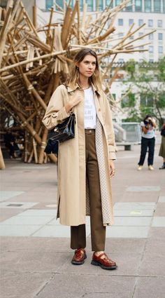 Woman in a trench coat and brown pants standing outdoors