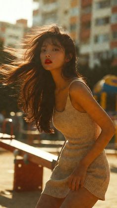 Woman with long hair and red lipstick in a beige dress outdoors at golden hour