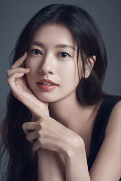 Woman with long black hair in a black top, posing with hands near her face
