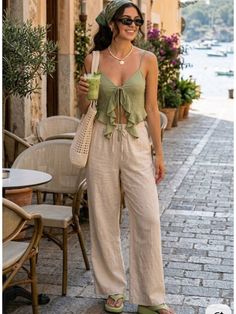 Woman in a green top and wide leg pants holding a drink on a street