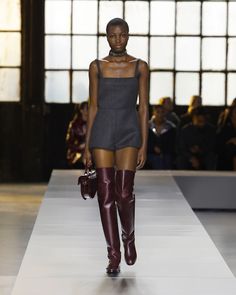 Model in a dark mini dress and over the knee boots on a runway