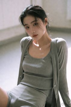 Woman with black hair wearing a grey cardigan and tank top indoors