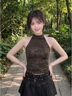 Woman in a leopard print top and black pleated skirt outdoors with green trees