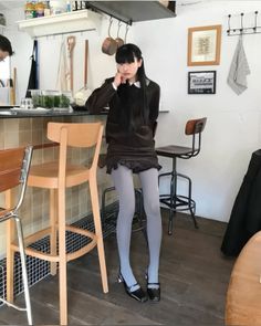 Woman with long black hair wearing a collared dress and tights in a cafe