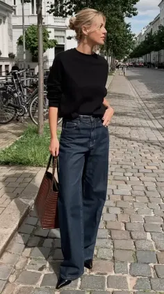 Woman with blonde hair in an updo wearing a black top and wide leg jeans on a cobblestone street