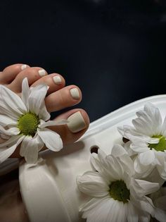 Foot with a light-colored pedicure and white daisies on a white sandal