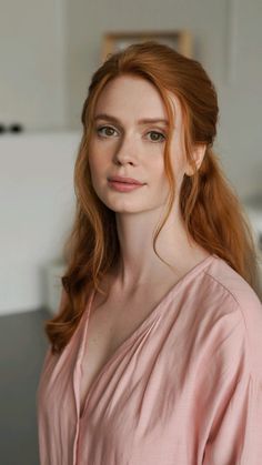 Woman with red hair and green eyes wearing a pink top indoors