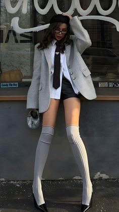 Woman in a blazer, black tie, and knee-high socks posing outdoors