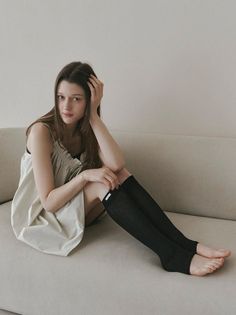 Woman with long hair sitting on a couch in a sleeveless dress and black socks