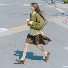 Woman in a green sweater and brown skirt crossing a street