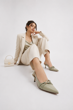 Woman in a light suit and green heels posing on a white background