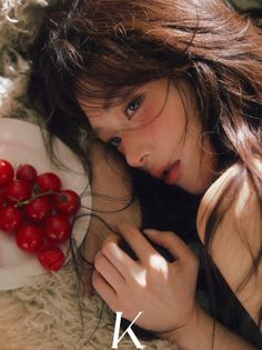 Woman with long hair and red blush lying down with cherry tomatoes