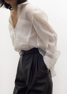 Person in a sheer white shirt and black pants with hands in pockets
