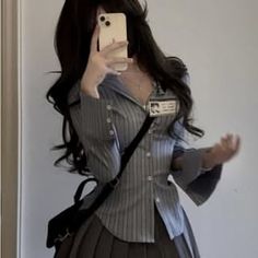 Person with long dark hair taking a mirror selfie in a striped shirt and pleated skirt