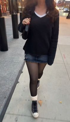 Woman in a black sweater and denim skirt walking on a street