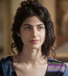 Woman with dark curly hair and green eyes wearing a striped shirt and blue hoodie
