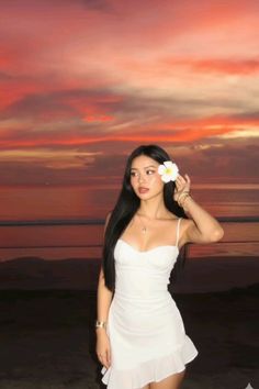 Woman in a white dress with a frangipani flower in her hair at sunset on a beach