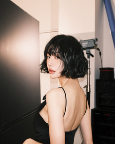 Woman with short black hair in a black dress looking over her shoulder