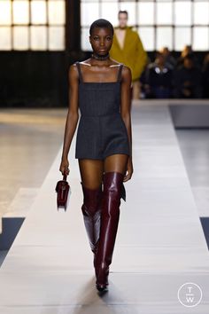 Model in a dark romper and thigh-high boots on a runway