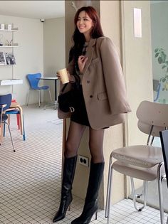 Woman in a blazer and black boots smiling in an indoor setting