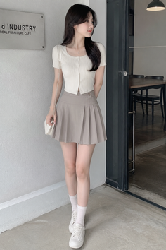 Woman in a white crop top and pleated skirt standing indoors