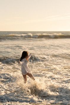 Woman in a white shirt playing in the ocean waves at golden hour