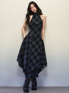 Woman in a plaid halter neck dress and black boots against a plain wall
