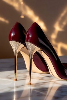 Pair of burgundy high heels with gold and rhinestone details on a marble surface