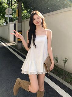 Woman in a white dress and brown boots posing on a street