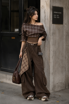 Woman in a plaid off-shoulder top and brown cargo pants holding a bag