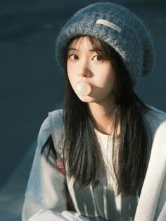 Young woman in a grey beanie blowing bubble gum outdoors